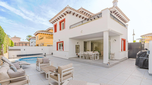 Image of a Mercia villa with white walls and dark orange accent colours around the windows and decorating the edge of the roof. There are beige chairs in the garden.